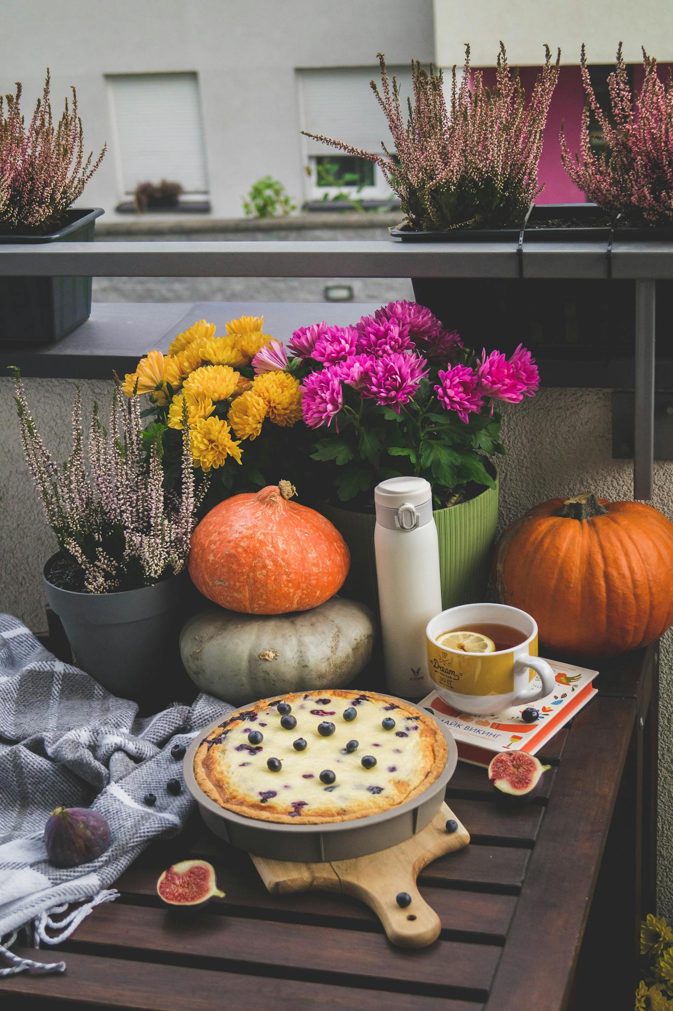 Cozy autumn table with blueberry dessert, pumpkins, tea, and flowers.