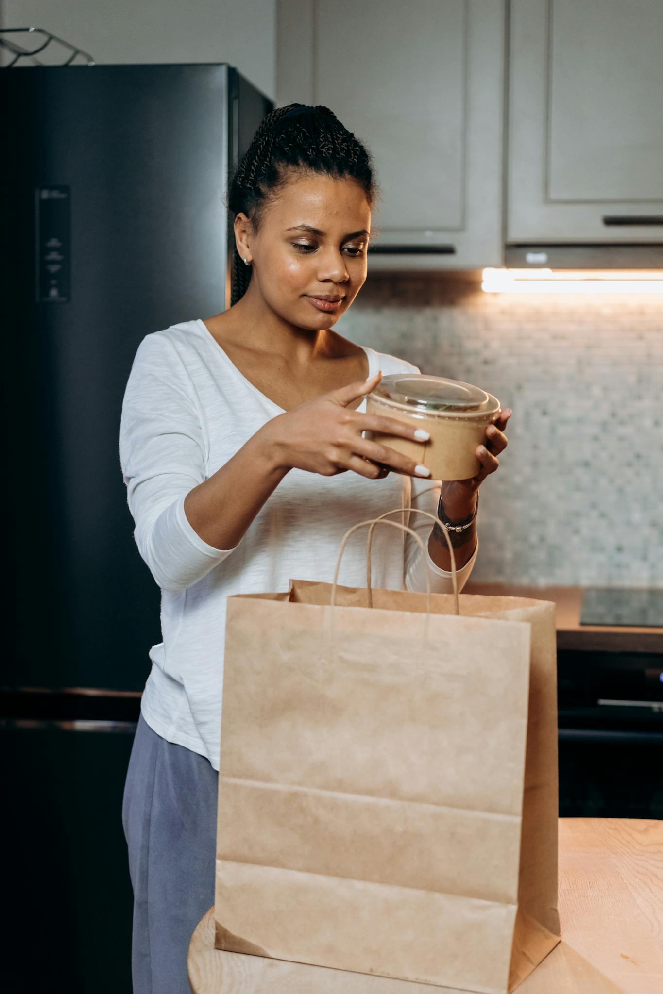 Woman in casual attire unpacking takeout food at home in a modern kitchen setting.